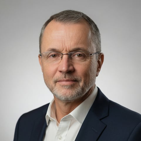 Professional headshot of a middle-aged man with gray hair and glasses wearing a dark blazer and white shirt